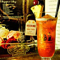 カクテルグラスに盛られた赤色のシンガポールスリング、パイナップルが添えてある