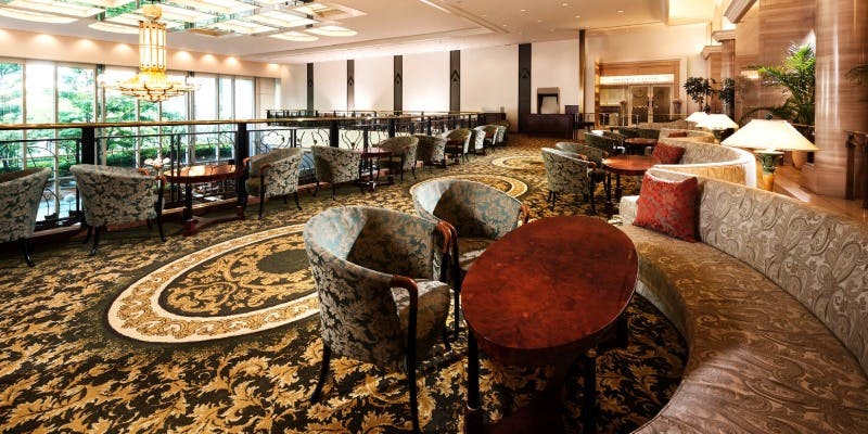 絨毯の敷かれたフロアに高級感のあるテーブル席が並ぶホテルのカフェ