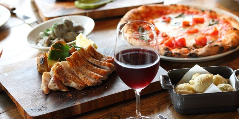 アダッキオの肉料理やピザ、ワインなどがテーブルの上に並んでいる様子