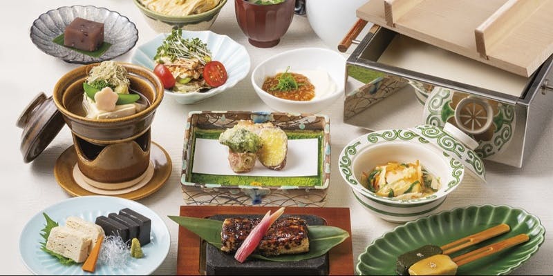 湯葉や豆腐を中心に彩り豊かに盛り付けられた料理。天ぷら、生麩田楽、豆腐料理、煮物、デザートなどが並ぶ豪華な和食膳