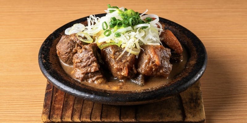 黒い皿に盛られてネギがのった牛すじ煮込み